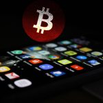 Celular com apps e símbolo do bitcoin no fundo